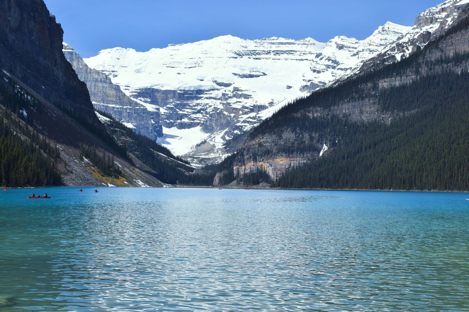 Les eaux turquoise du lac Louise reflètent les montagnes boisées environnantes et les sommets enneigés du mont Victoria dans le parc national de Banff.