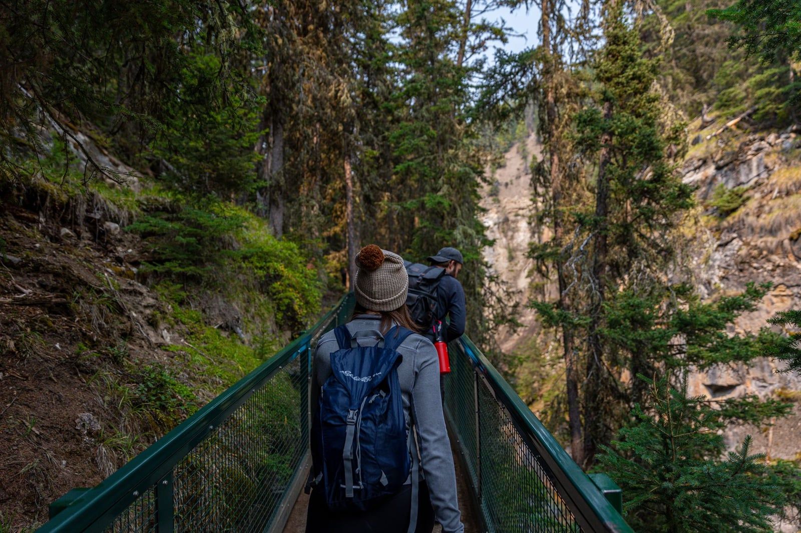 Des randonneurs avec des sacs à dos marchent le long d'un sentier sur passerelle à rampe dans le Johnston Canyon, dans le parc national de Banff.