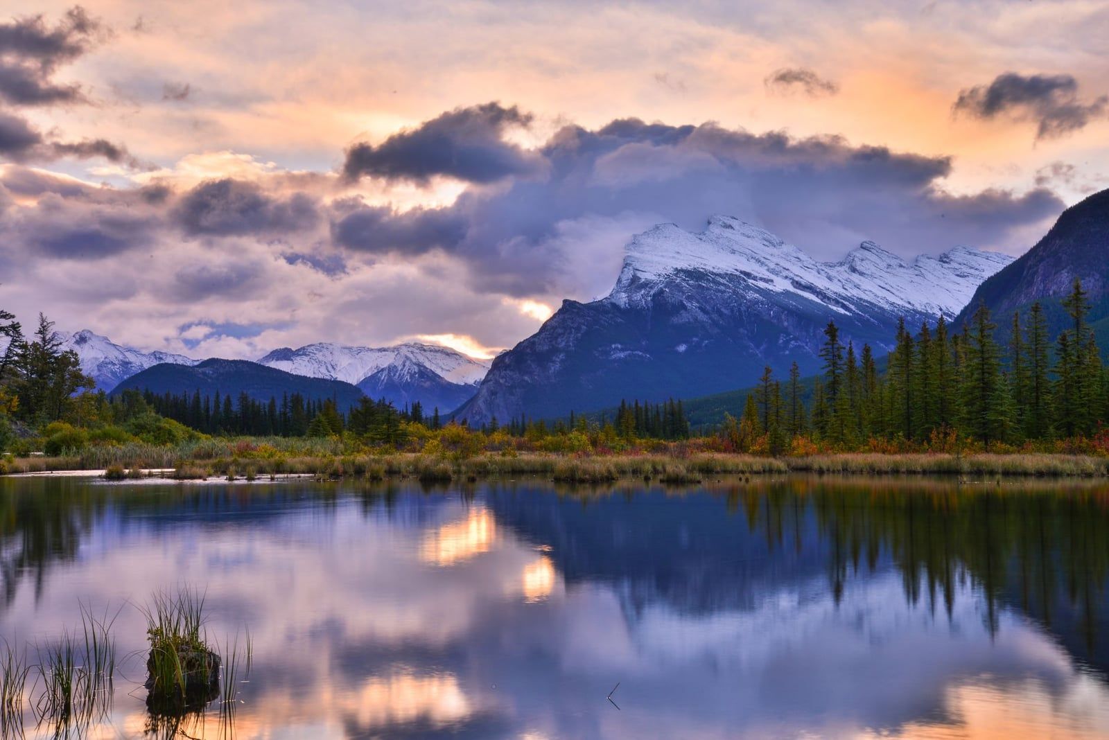 Le mont Rundle saupoudré de neige et les nuages colorés du lever du soleil se reflètent sur la surface calme des lacs Vermilion dans le parc national de Banff.