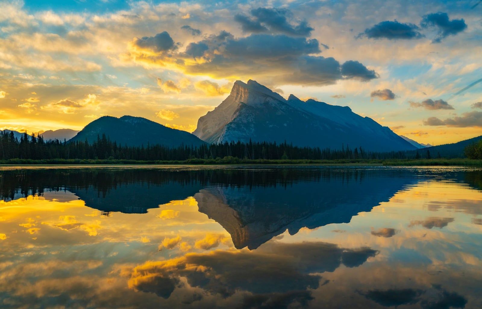 Le mont Rundle et les nuages dorés du coucher du soleil se reflètent dans les eaux calmes des lacs Vermilion dans le parc national de Banff.