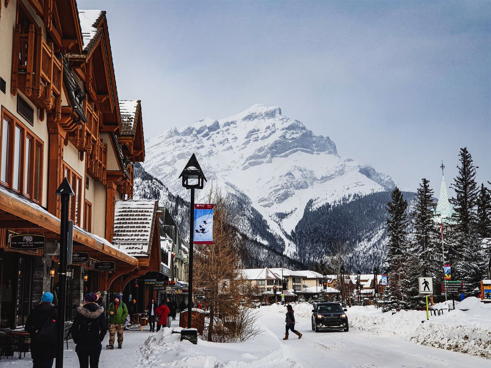 Peatones caminan junto a escaparates cubiertos de nieve en Banff Avenue con el monte Cascade nevado alzándose al fondo en el Parque Nacional Banff.