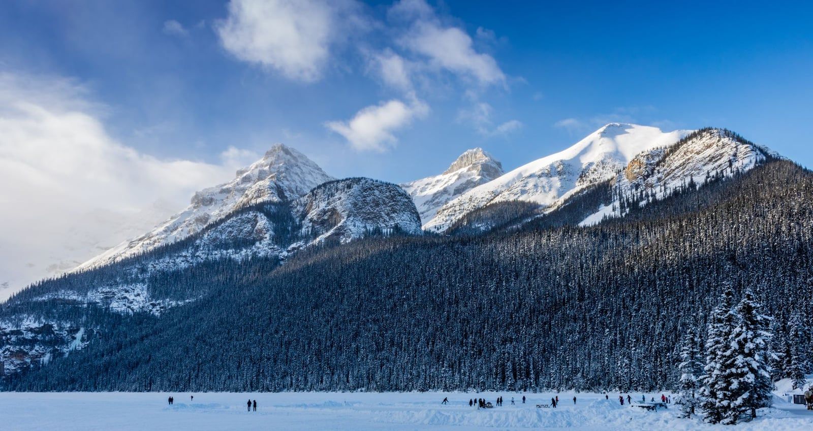 Unos patinadores se deslizan por la superficie helada del lago Louise con un telón de fondo de montañas nevadas en el Parque Nacional Banff.