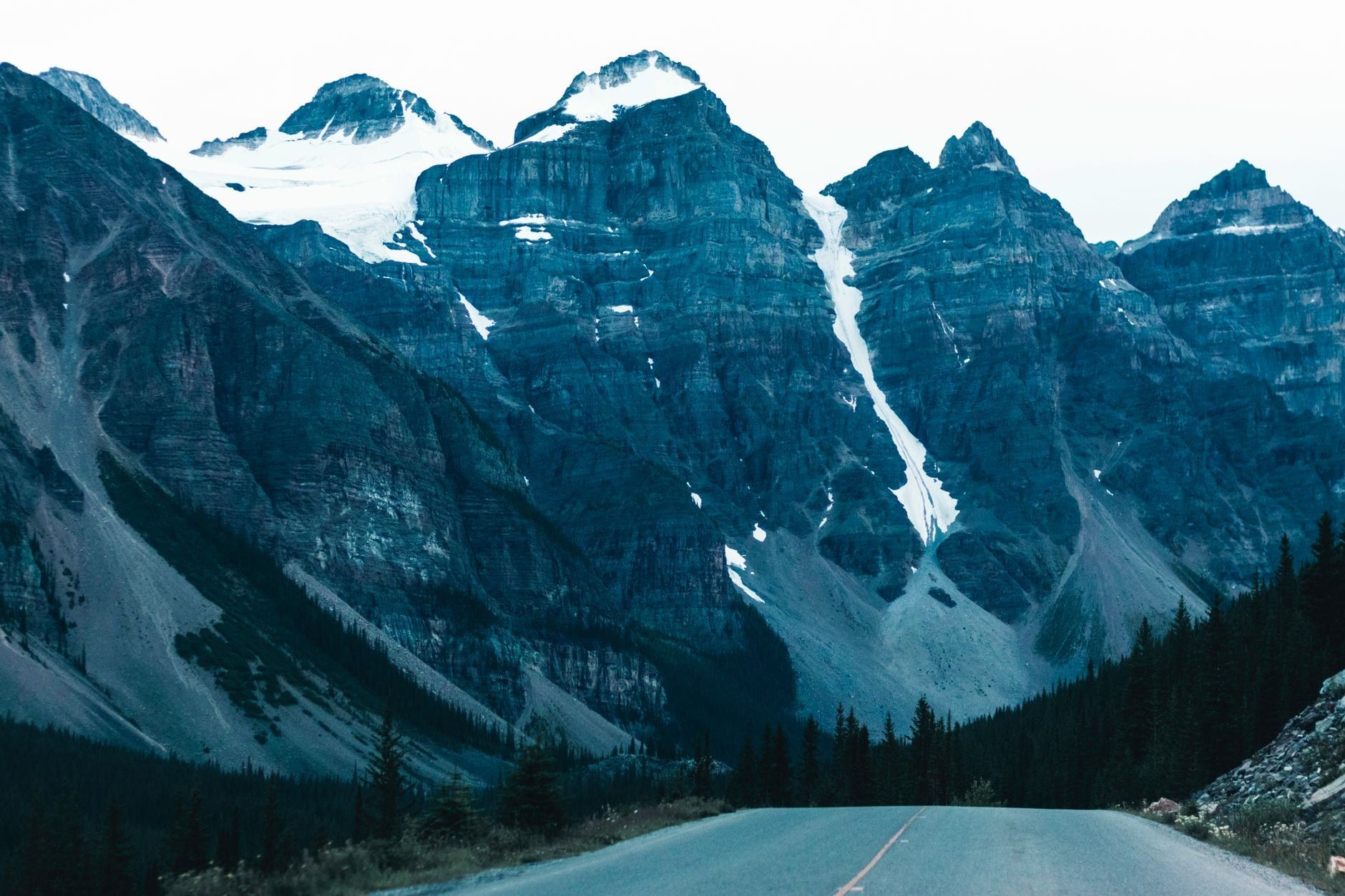 A paved highway leads toward towering, snow-dusted mountain peaks in Banff National Park.