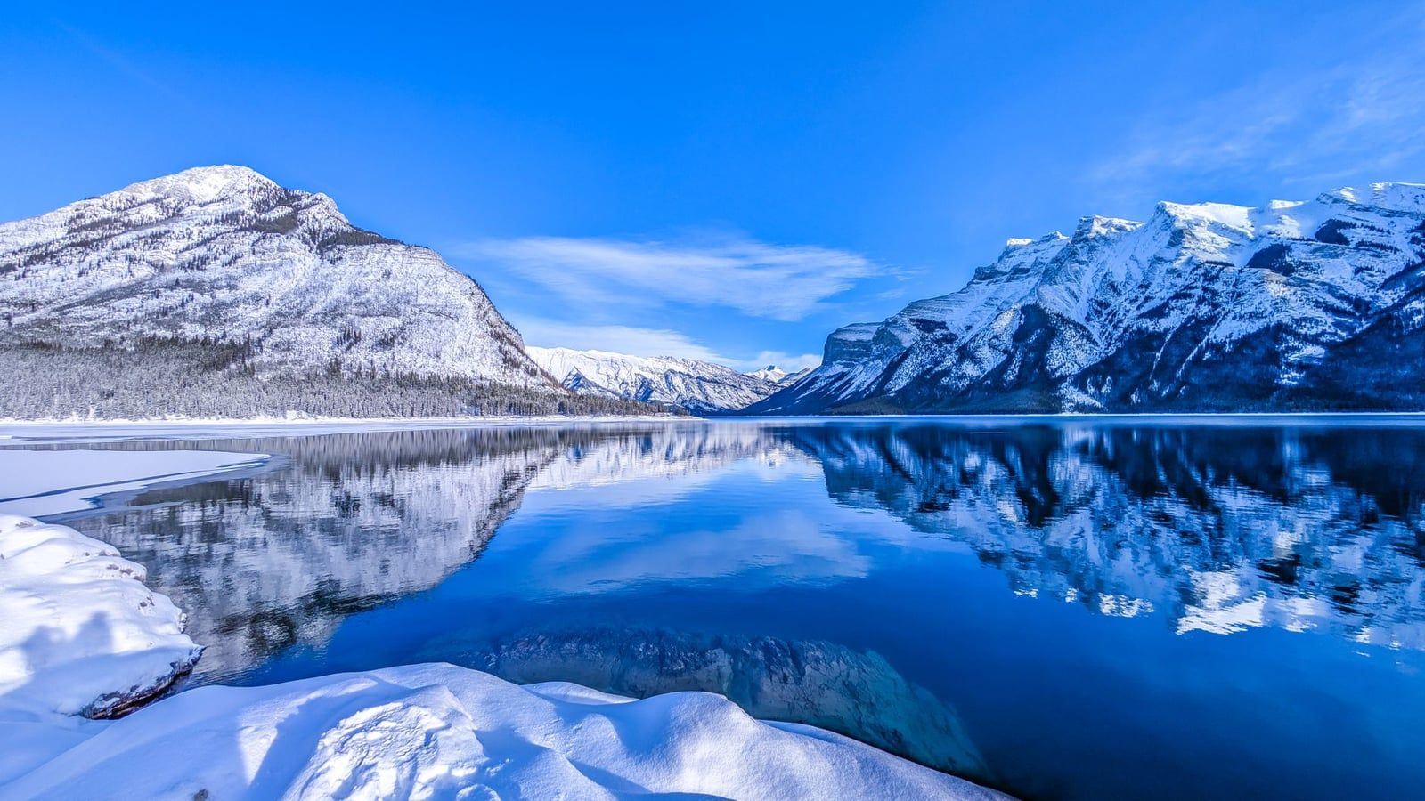 Las Montañas Rocosas cubiertas de nieve se reflejan en las aguas tranquilas y parcialmente congeladas del lago Minnewanka, en el Parque Nacional de Banff.