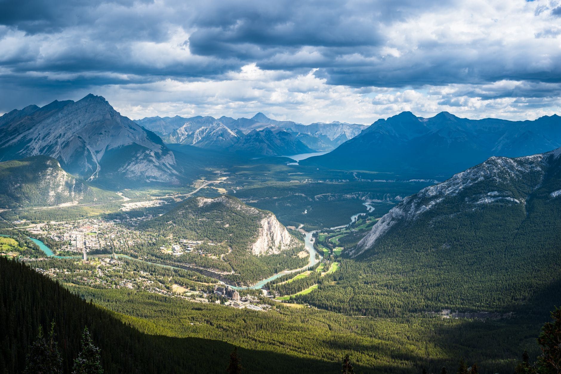 Panoramic view of the town of Banff and the winding Bow River surrounded by forested valleys and rugged mountain peaks in Banff National Park.