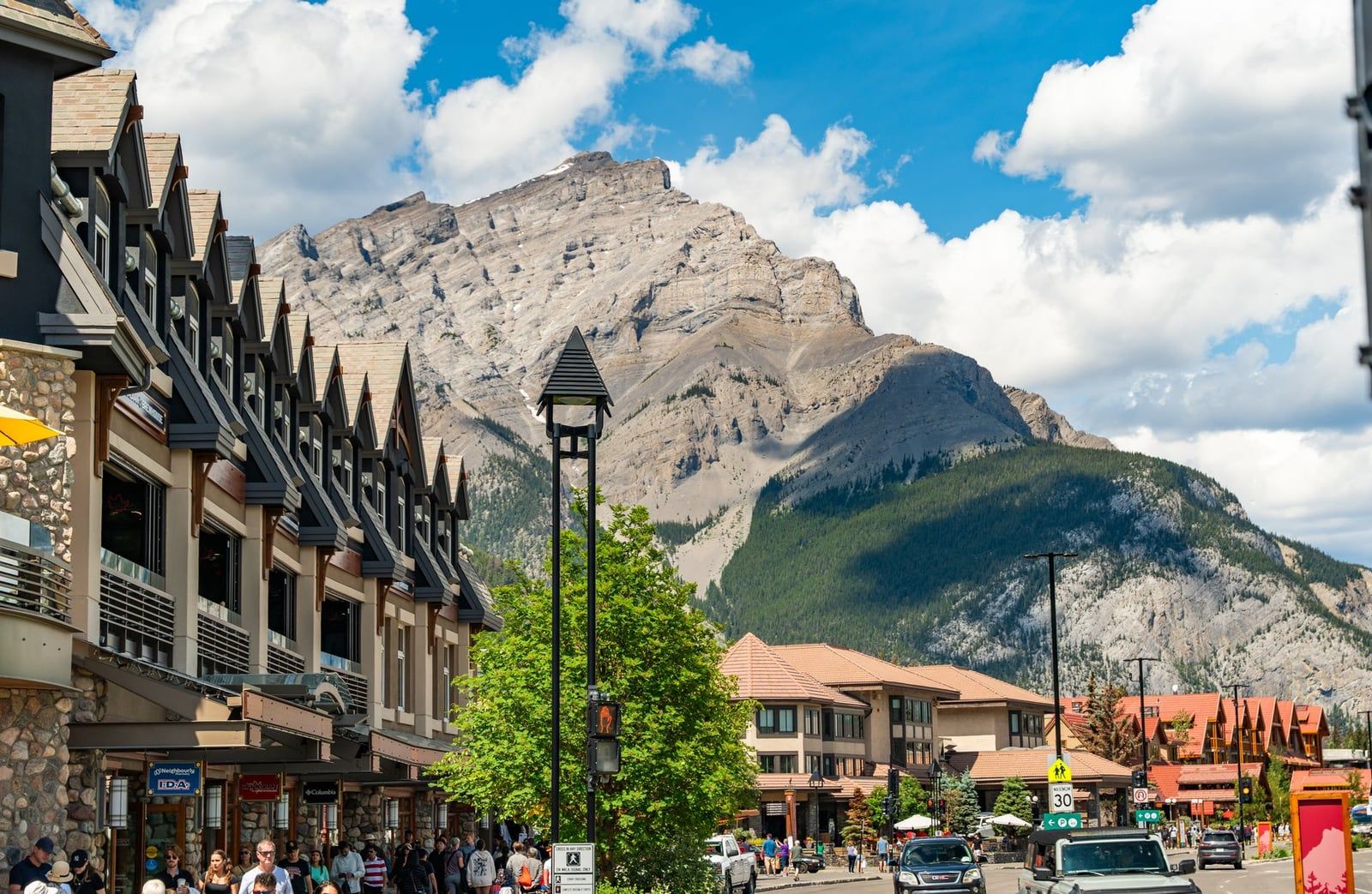 Fußgänger gehen an Geschäften entlang der Banff Avenue vorbei, unter dem aufragenden Gipfel des Cascade Mountain im Banff National Park.